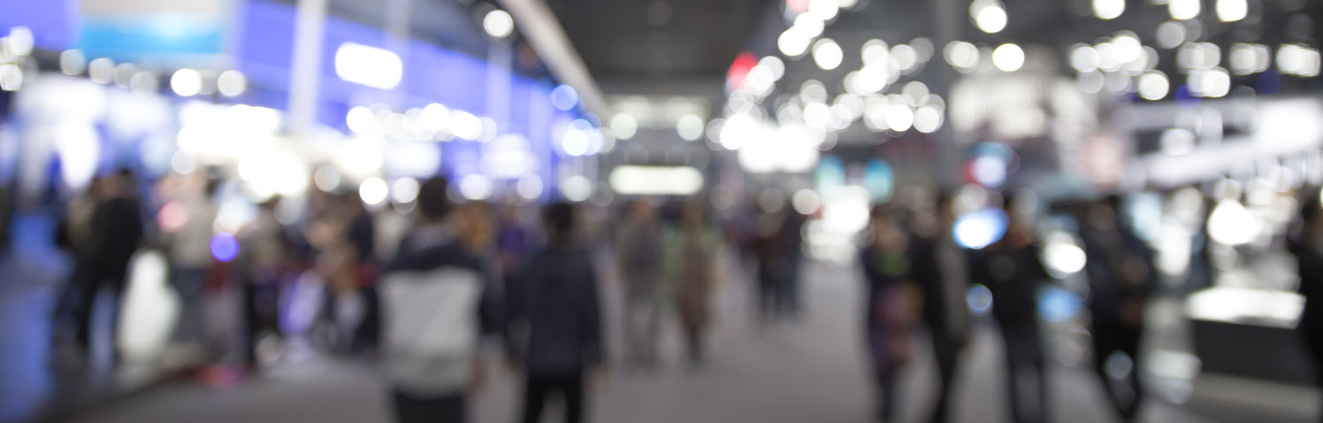 A defocused image of an exhibition hall floor with people moving along a wide walkway.